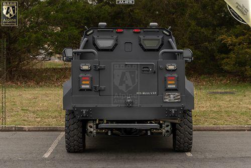 A rear view of a black armored Pit-Bull VXT parked in a lot, featuring thick tires and various lighting and safety components.