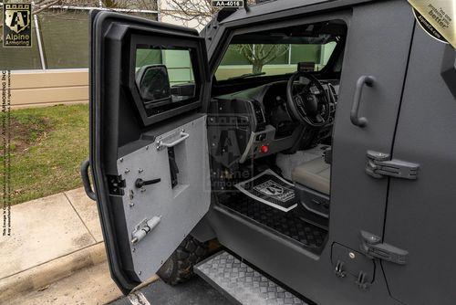 The image shows the open driver's side door of a rugged, armored Pit-Bull VXT. The vehicle features a reinforced interior with an upholstered seat and a detailed dashboard.