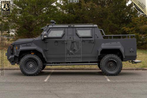 A matte black armored Pit-Bull VXT from Alpine Armoring parked on a road, viewed from the side, showcasing its robust build and rugged tires.