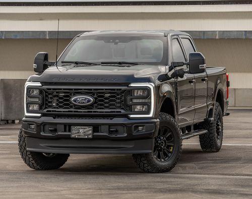 A black Ford Super Duty F-350 Lariat pickup truck is parked on a concrete surface in front of a multi-story building.