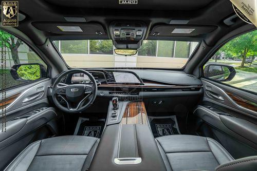 Interior view of an armored Cadillac Escalade ESV car showing a leather-wrapped dashboard, steering wheel, and seats, with wood trim details and advanced control panels.