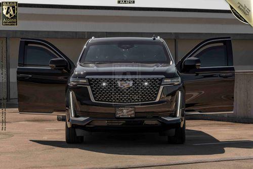 Front view of an armored Cadillac Escalade ESV SUV with both front doors open, displaying the vehicle's grille and headlights. The SUV is parked in an outdoor lot.