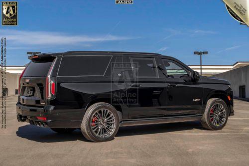 A black armored Cadillac Escalade ESV SUV is parked in an outdoor lot. The vehicle is customized by Alpine Armoring Inc. and features tinted windows and detailed branding.