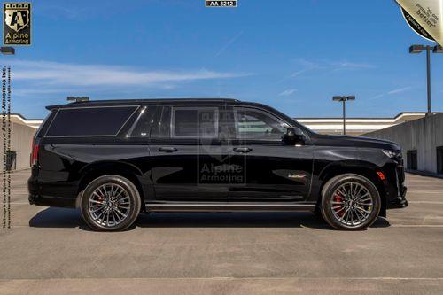 Passenger side view of a black Cadillac Escalade ESV SUV is parked in an outdoor parking lot with an empty rooftop background.