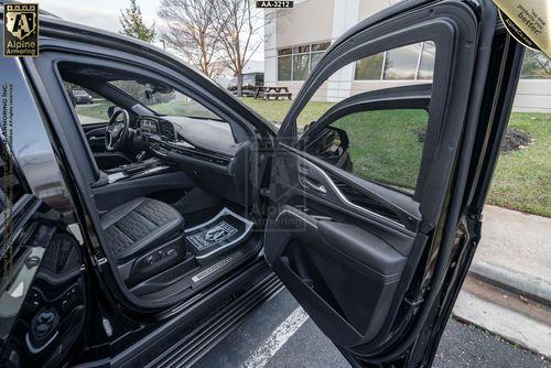 Open rear passenger door of a black armored Cadillac Escalade ESV SUV showing the interior and exterior of the vehicle parked in front of a modern building.