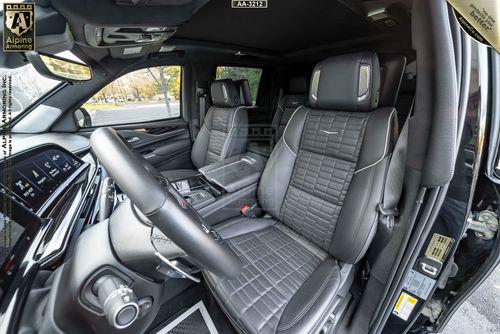 Interior of a luxurious armored Cadillac Escalade ESV SUV with black leather seats featuring intricate stitching, a modern dashboard, and various controls and displays.