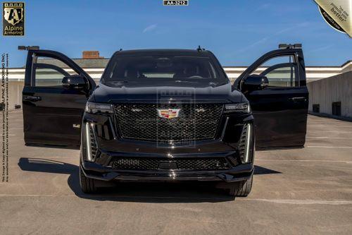 A black bulletproof Cadillac Escalade ESV SUV  is parked in a rooftop lot with its front doors open. The vehicle is viewed from the front with a clear view of its grille and logo.