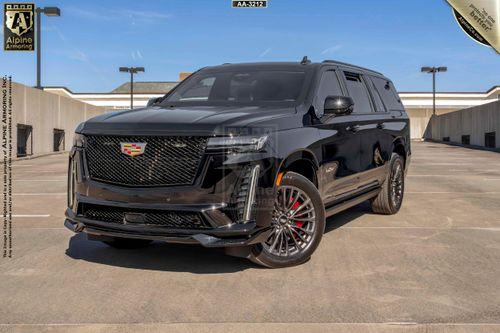 A black Cadillac Escalade ESV SUV is parked in an outdoor parking lot with an empty rooftop background.